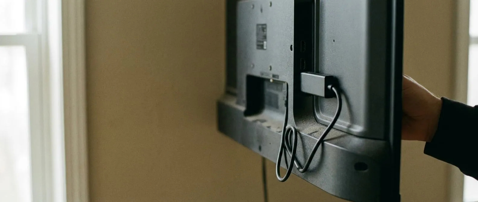 A small streaming stick being plugged into the HDMI port at the back edge of a wall-mounted television.