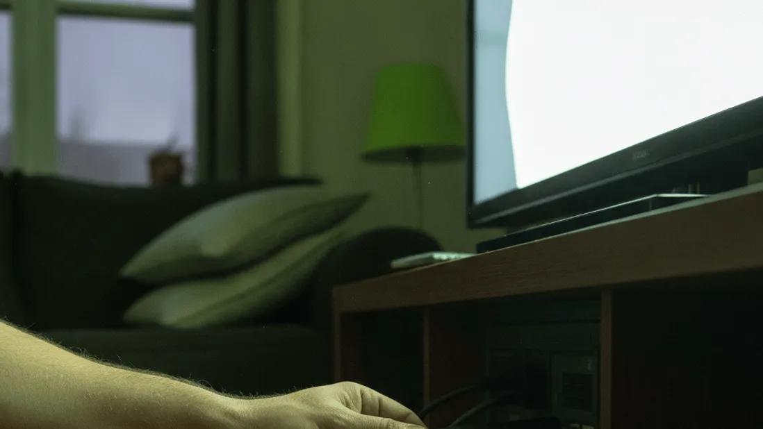 A man's hand inserts a streaming stick into an HDMI port on a television in a dimly lit living room.